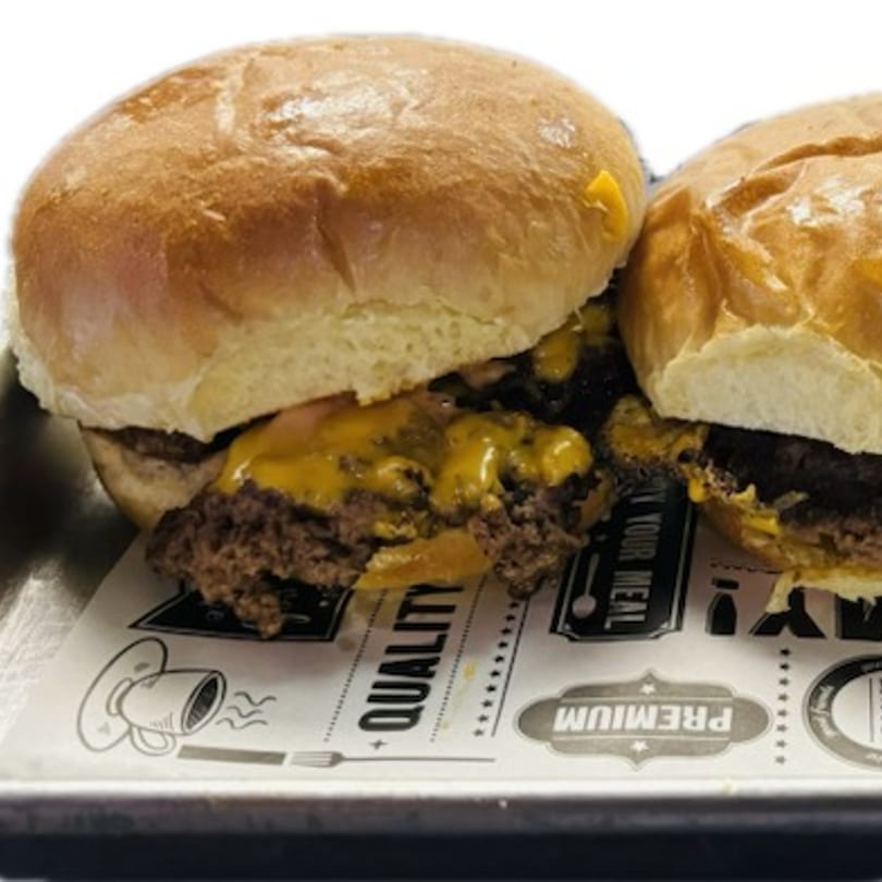 Two cheesy smash burgers on a tray with branded paper from Roll-out Wingz & Eggrolls.