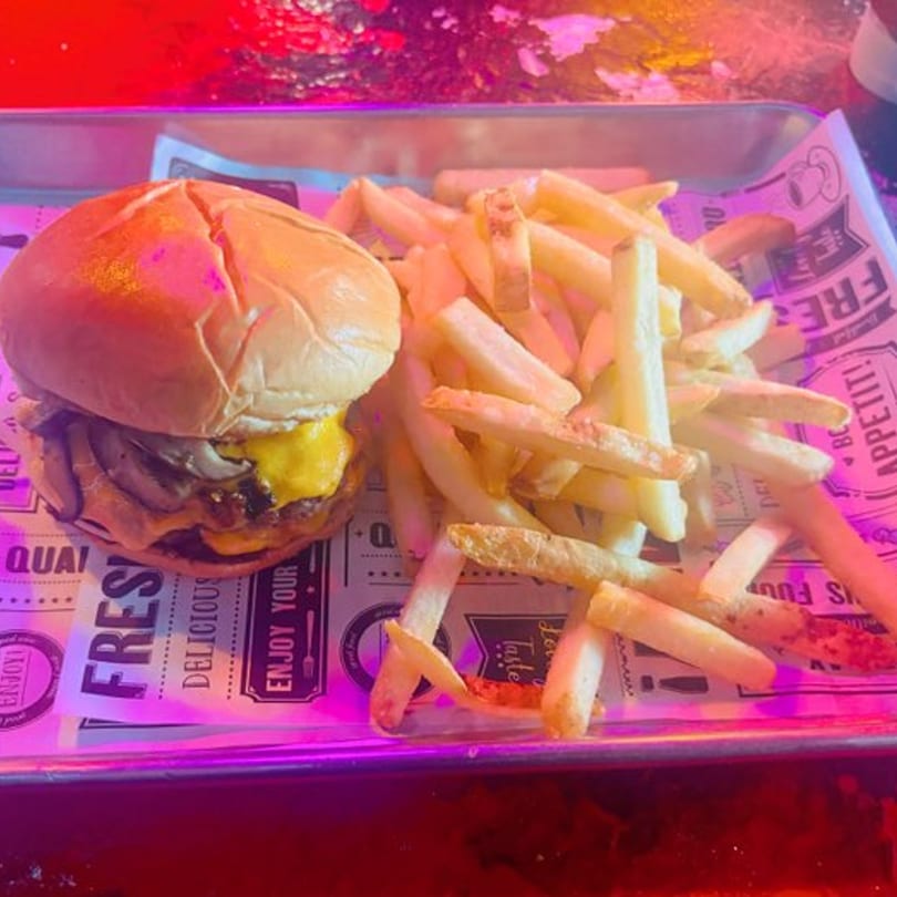 A cheeseburger with mushrooms and a side of french fries on a metal tray with patterned paper.